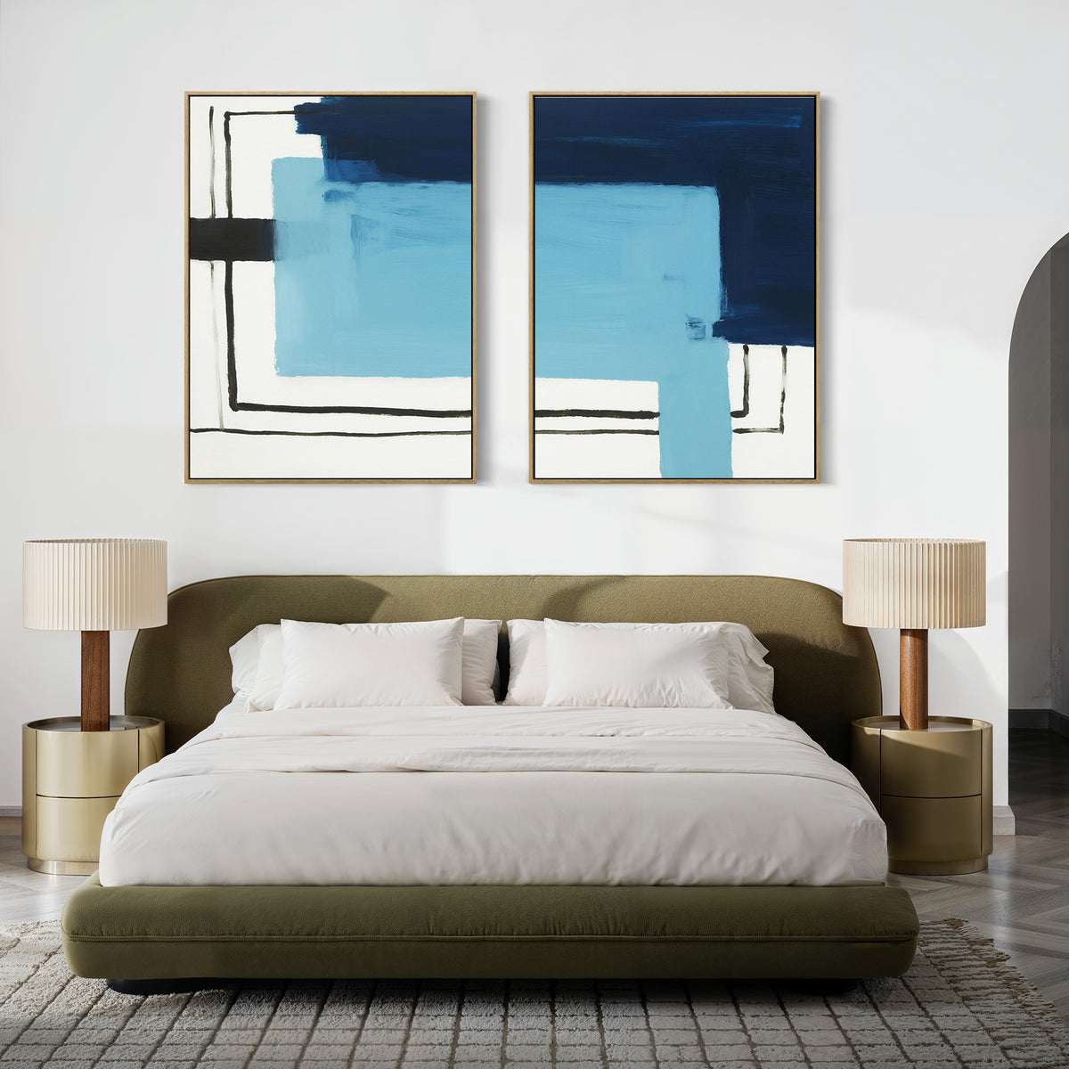 A modern bedroom with a low olive-green bed, white bedding, gold nightstands with beige lamps, and the "Cobalt Intersection - Set Of 2" abstract art set, adding a modern decor touch to the white wall above the bed.