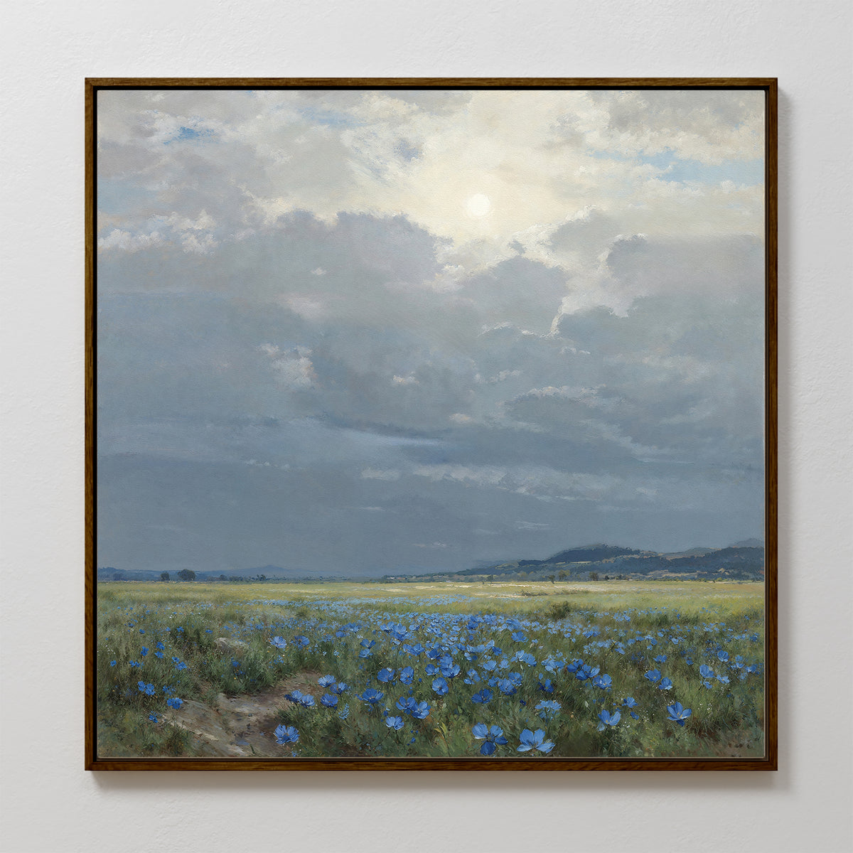 The Cornflower Fields Canvas Art - Square features a framed landscape of grassy fields and blue wildflowers beneath a cloudy sky with distant hills—perfect countryside wall art for a tranquil atmosphere.