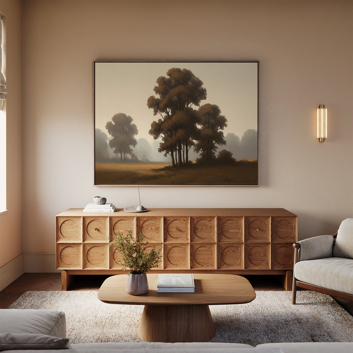 A cozy living room features a light sofa, wooden coffee table, and textured sideboard topped with a lamp and vase. Above the sideboard hangs the 'Dawn Silhouettes Canvas Art - Horizontal' print, showcasing serene trees.