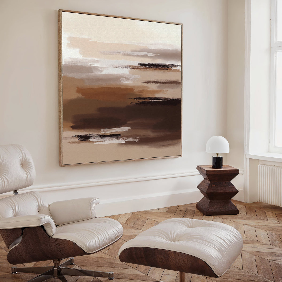 A modern living room with a white leather lounge chair and ottoman, wooden side table with a white lamp, and the Desert Winds Canvas Art - Square above. Light wood herringbone floors and a large window complete the serene space.