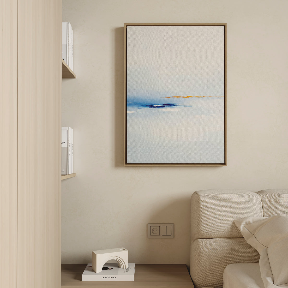 A modern living room corner with a beige sofa, minimalist shelves, a small geometric sculpture, and the Distant Archipelago Canvas Art - Vertical in blue and gold tones framed on a light wall.