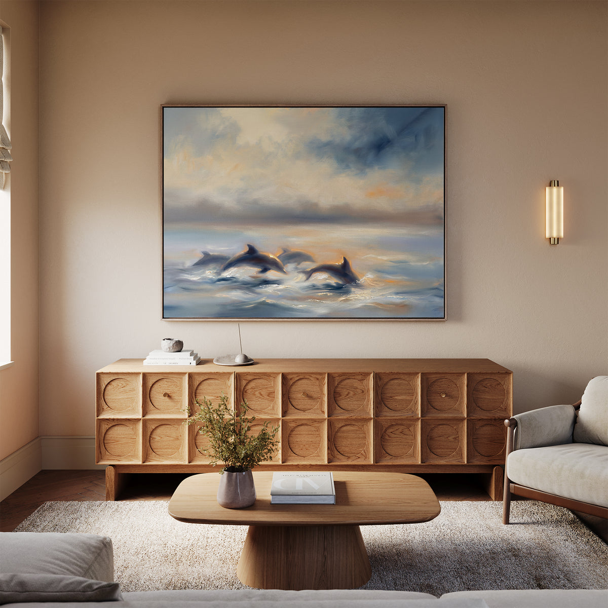 A cozy living room with neutral tones, featuring a wooden sideboard, coffee table with a book and vase, light-colored sofa, and the Dolphin Pod at Sunset Canvas Art - Horizontal as calming coastal wall decor above the sideboard.