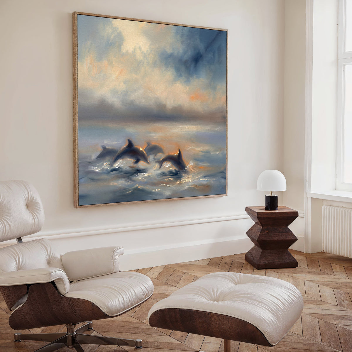 A modern living room features a white leather chair and ottoman, a wooden side table with a small lamp, and serene wall art—a Dolphin Pod at Sunset Canvas Art - Square displayed on the wall.