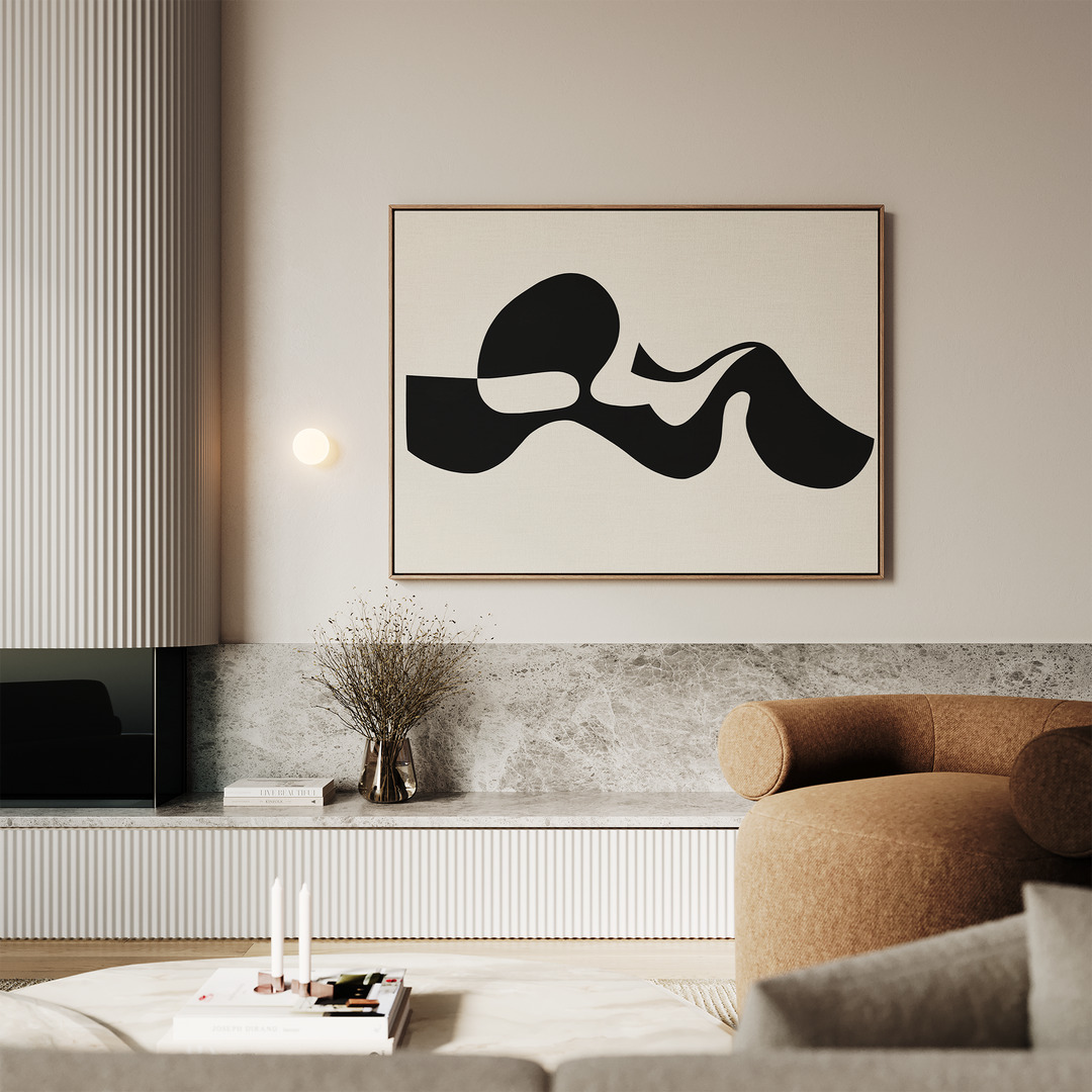 A modern living room with a beige sofa, stone accents, a low table with books and candles, and Fluid Forms Abstract Canvas Art in black and white above the sofa; a vase with dried flowers sits on a shelf.