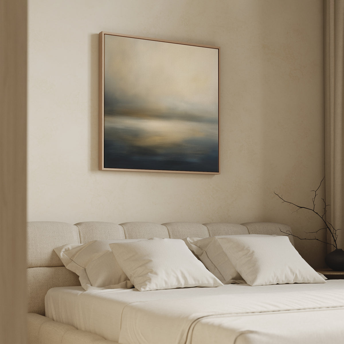 A minimalist bedroom features a beige upholstered bed with white bedding and the Foggy Bay Impressions Canvas Art - Square in soft blue, gray, and beige tones above the headboard. A bare branch in a vase sits on the nightstand.