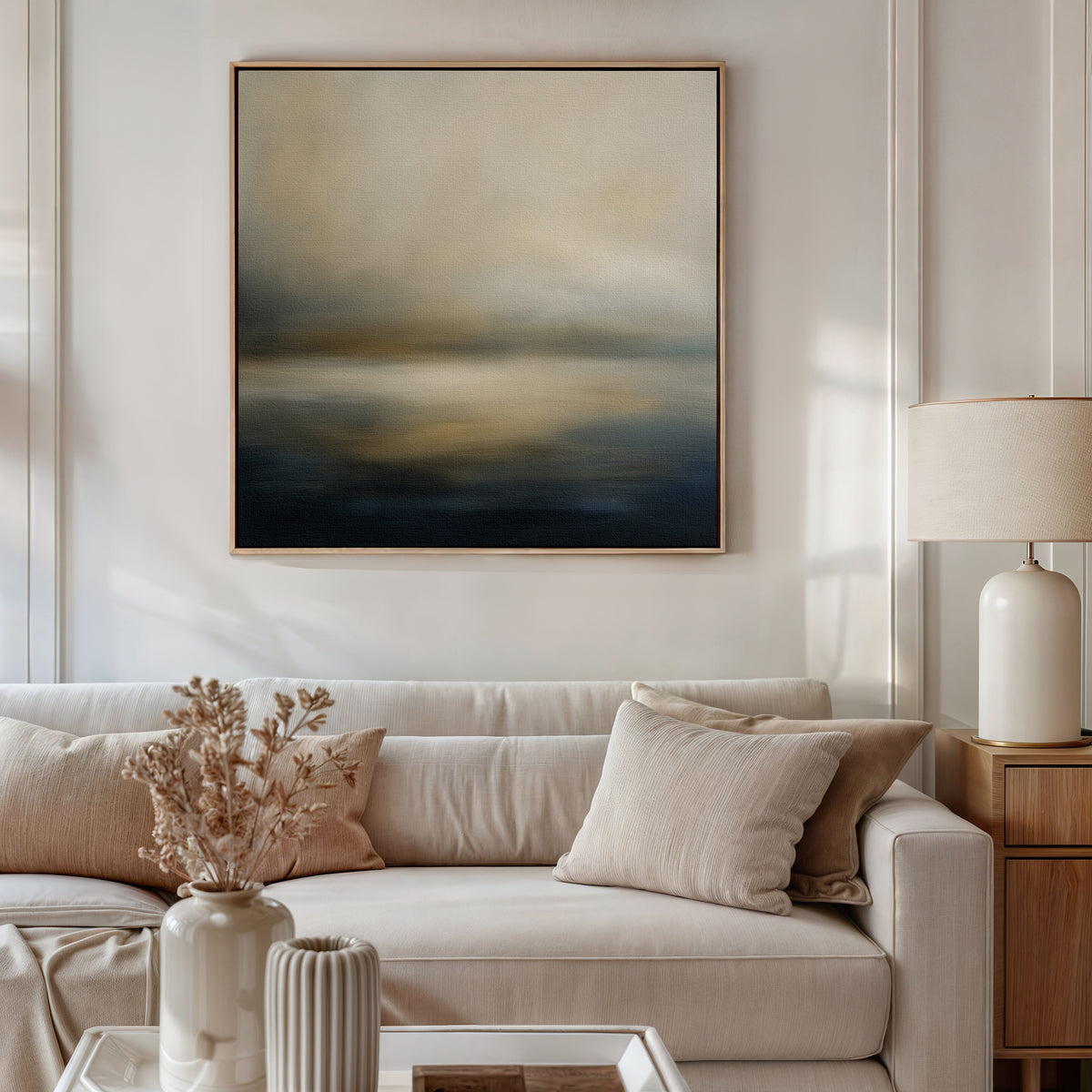 A modern living room with a beige sofa, neutral cushions, dried flowers in vases on a coffee table, a table lamp, and the Foggy Bay Impressions Canvas Art—square wall art with soft muted tones—brings Nordic Park tranquility to the space.