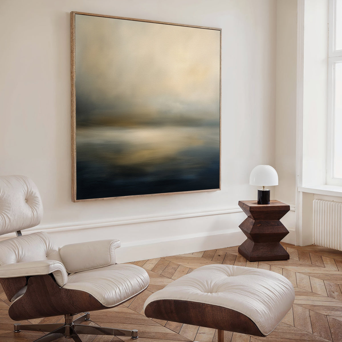 A modern living room featuring a white leather lounge chair with ottoman, a wooden side table with a small white lamp, and the Foggy Bay Impressions Canvas Art - Square brings Nordic Park-inspired tranquility to the space.