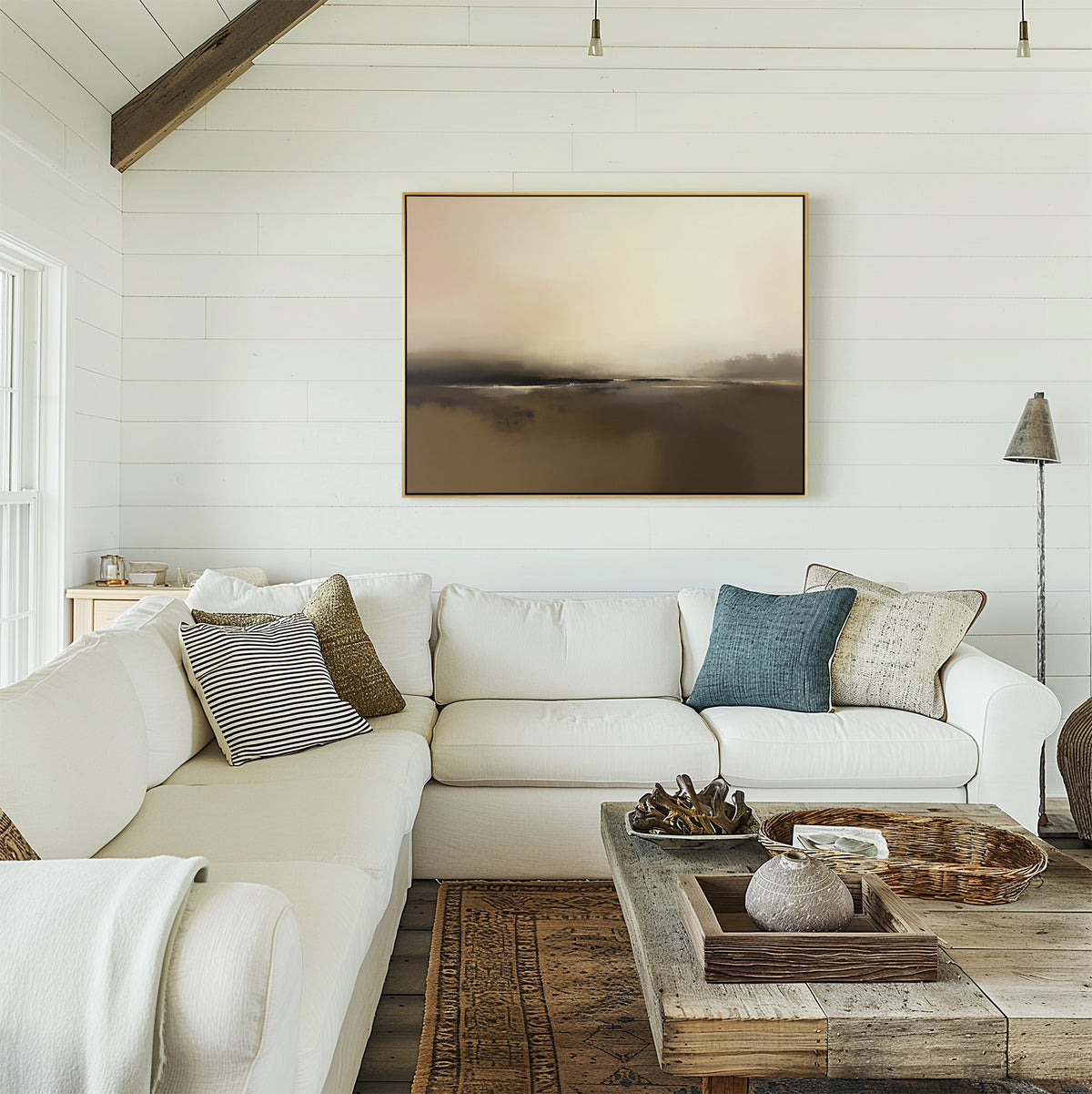 A cozy living room with white shiplap walls, a large white sectional sofa with patterned pillows, a rustic wooden coffee table, and serene coastal decor featuring the Foggy Beach Expanse Canvas Art - Horizontal above the sofa.