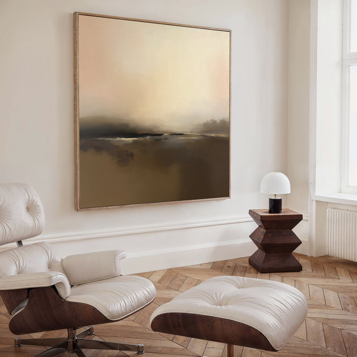 A modern living room featuring a white leather lounge chair and ottoman, a geometric wooden side table with lamp, and Nordic decor highlighted by the Foggy Beach Expanse Canvas Art - Square on the wall.