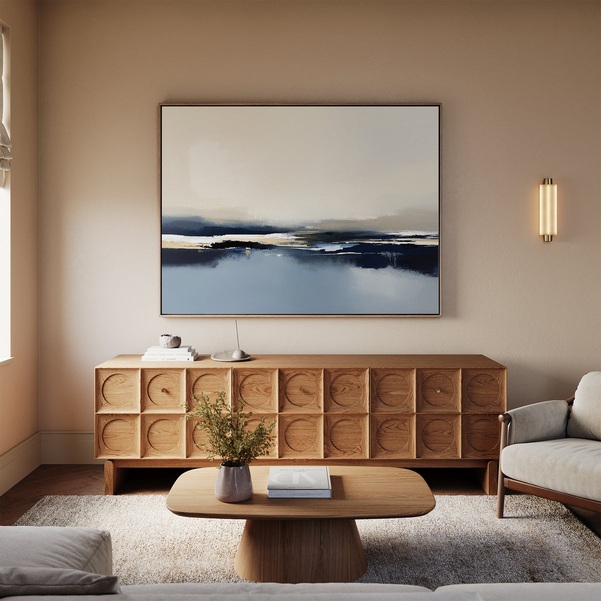 A modern living room features a wooden coffee table, textured sideboard, neutral-toned sofa, and the Frozen Bay Canvas Art - Horizontal, a large contemporary print in blue and white. A small vase with flowers sits on the table.