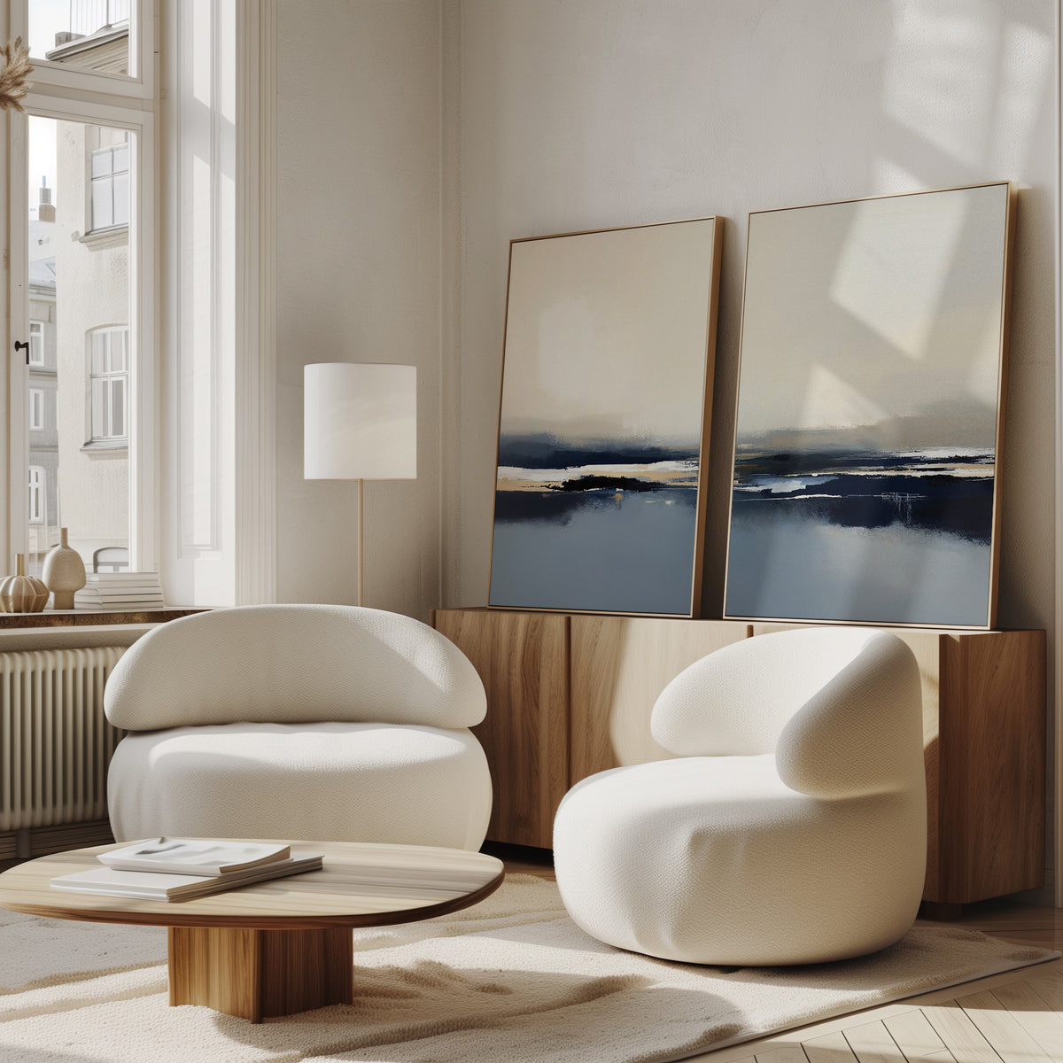A modern living room features Frozen Bay - Set Of 2 white curved armchairs, a round wooden coffee table, and a wooden sideboard with abstract art. Large windows fill the space with natural light for stylish decor.