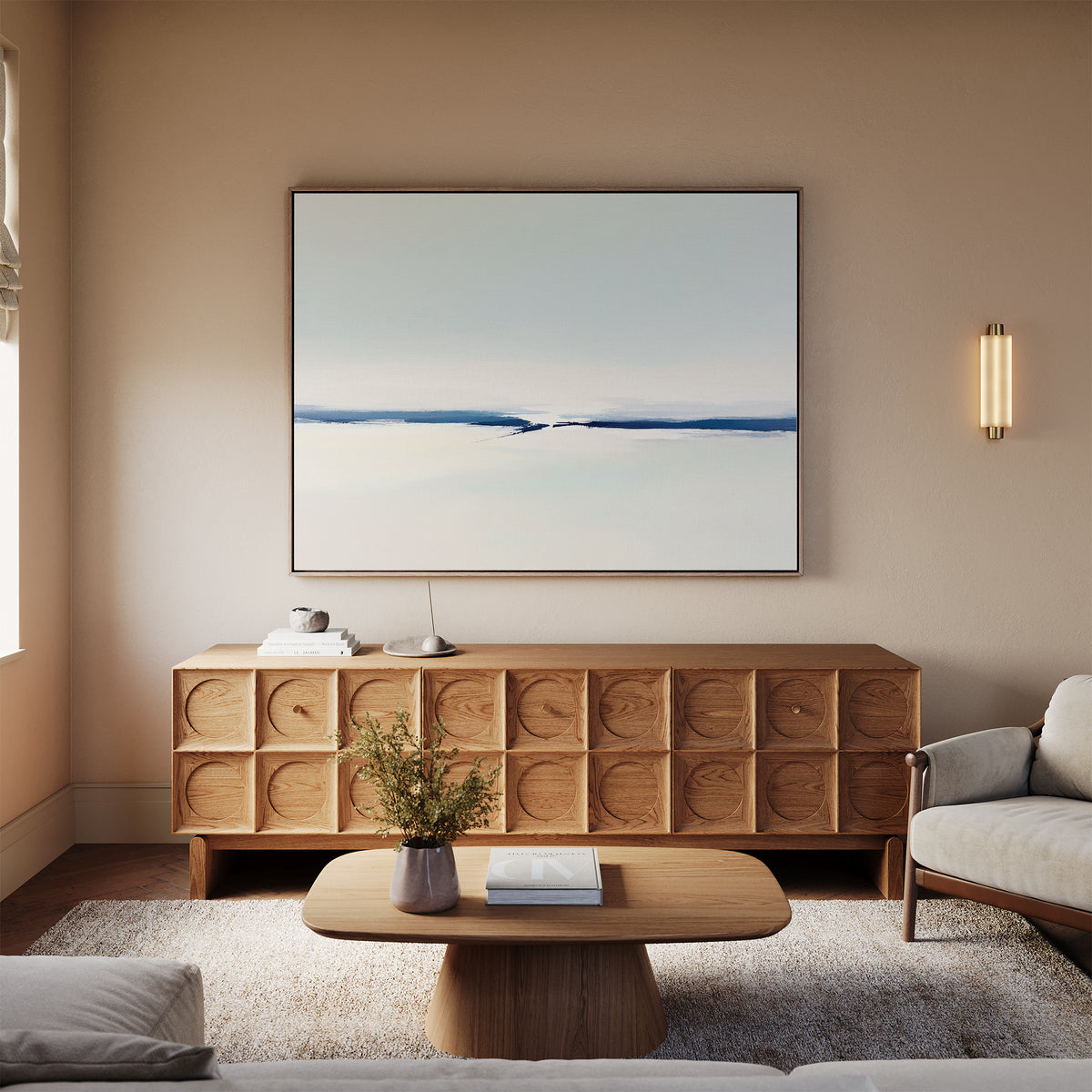 A minimalist living room with a light wood coffee table, matching sideboard, beige sofa, neutral rug, wall-mounted light, and the Frozen Channel Canvas Art - Horizontal in soft blue and white tones above the sideboard for modern decor.