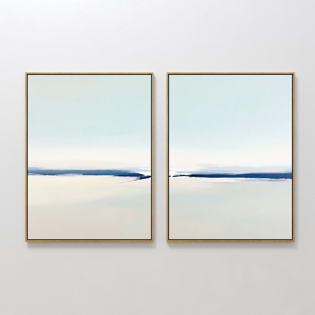 Frozen Channel - Set Of 2 features two minimalist wall art prints with thin gold frames and soft blue and off-white gradients, evoking calm water and sky—ideal for modern living room decor.