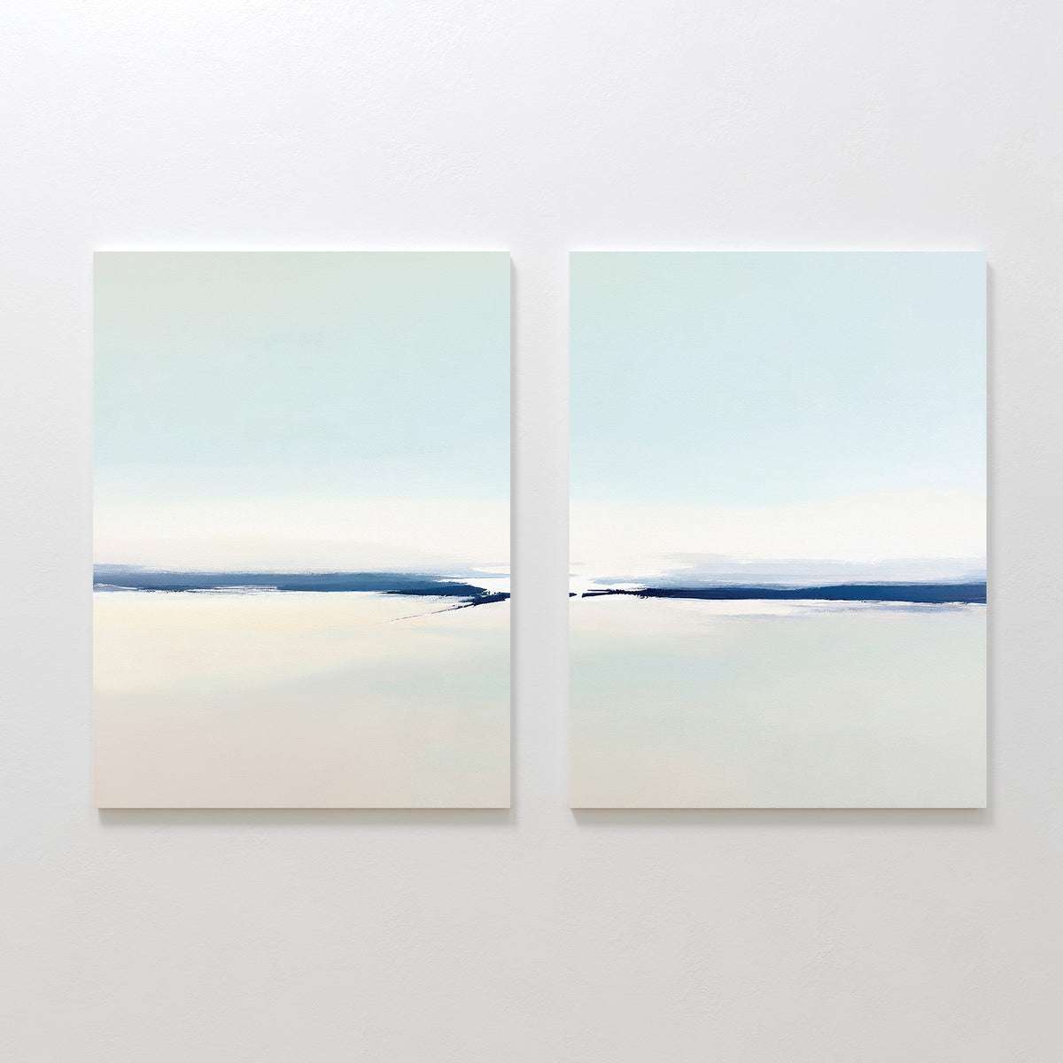 Frozen Channel - Set Of 2 features minimalist wall art with soft, blurred horizontal bands of light blue, white, and beige—ideal serene prints for modern living room decor against a white wall.
