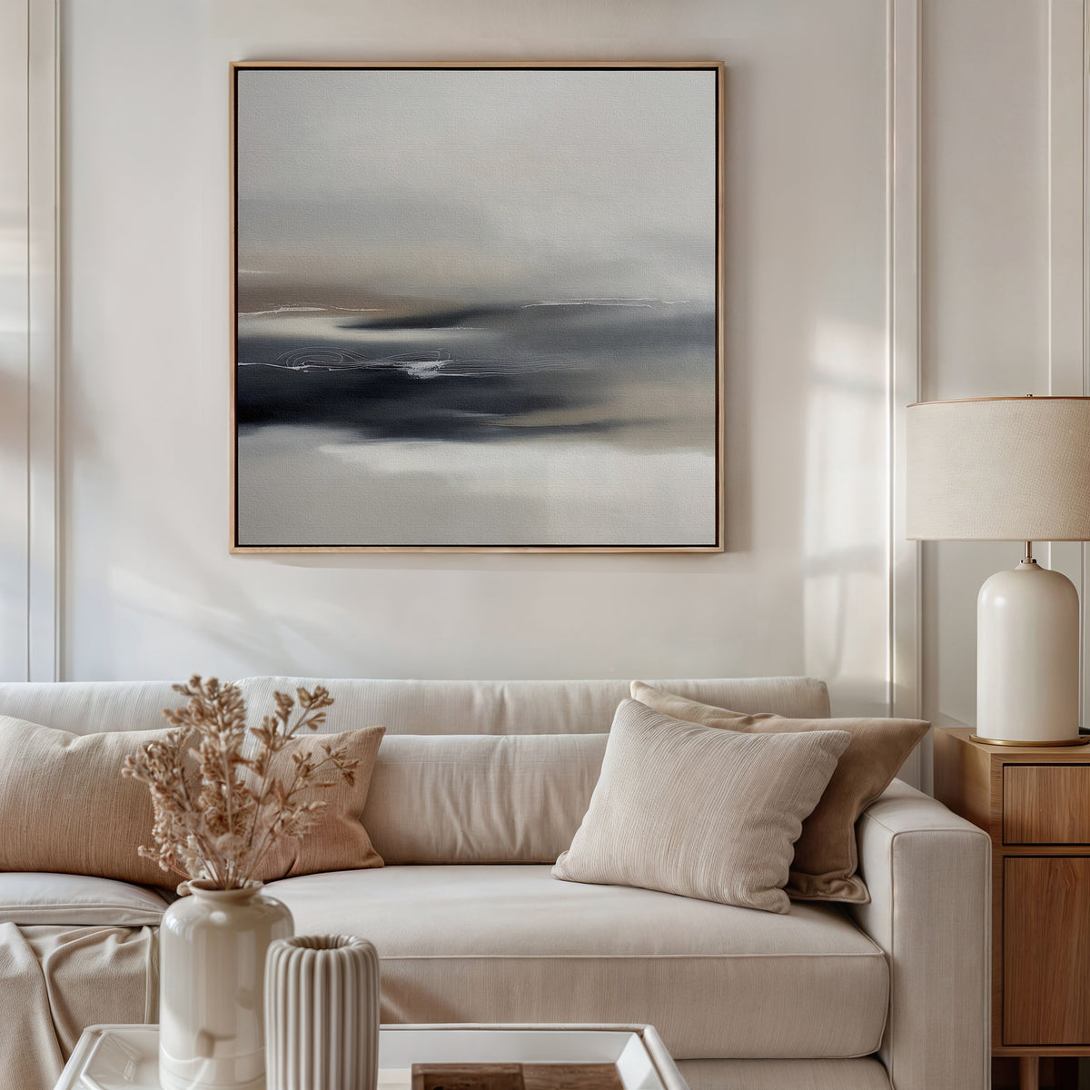 A modern living room featuring a beige sofa, neutral cushions, wooden side table with ceramic lamp, dried flowers in a vase, and the Grey Ripples Canvas Art - Square on the wall—ideal for fans of modern design.