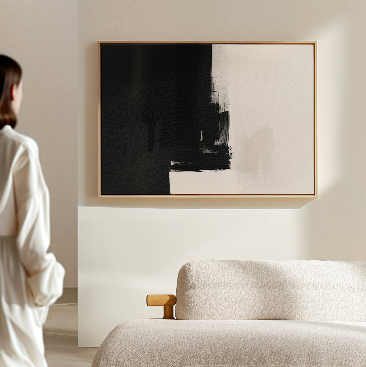 A person in a white shirt stands in a modern, minimal living room, admiring the Ink Divide Canvas Art - Horizontal displayed above a light-colored sofa.