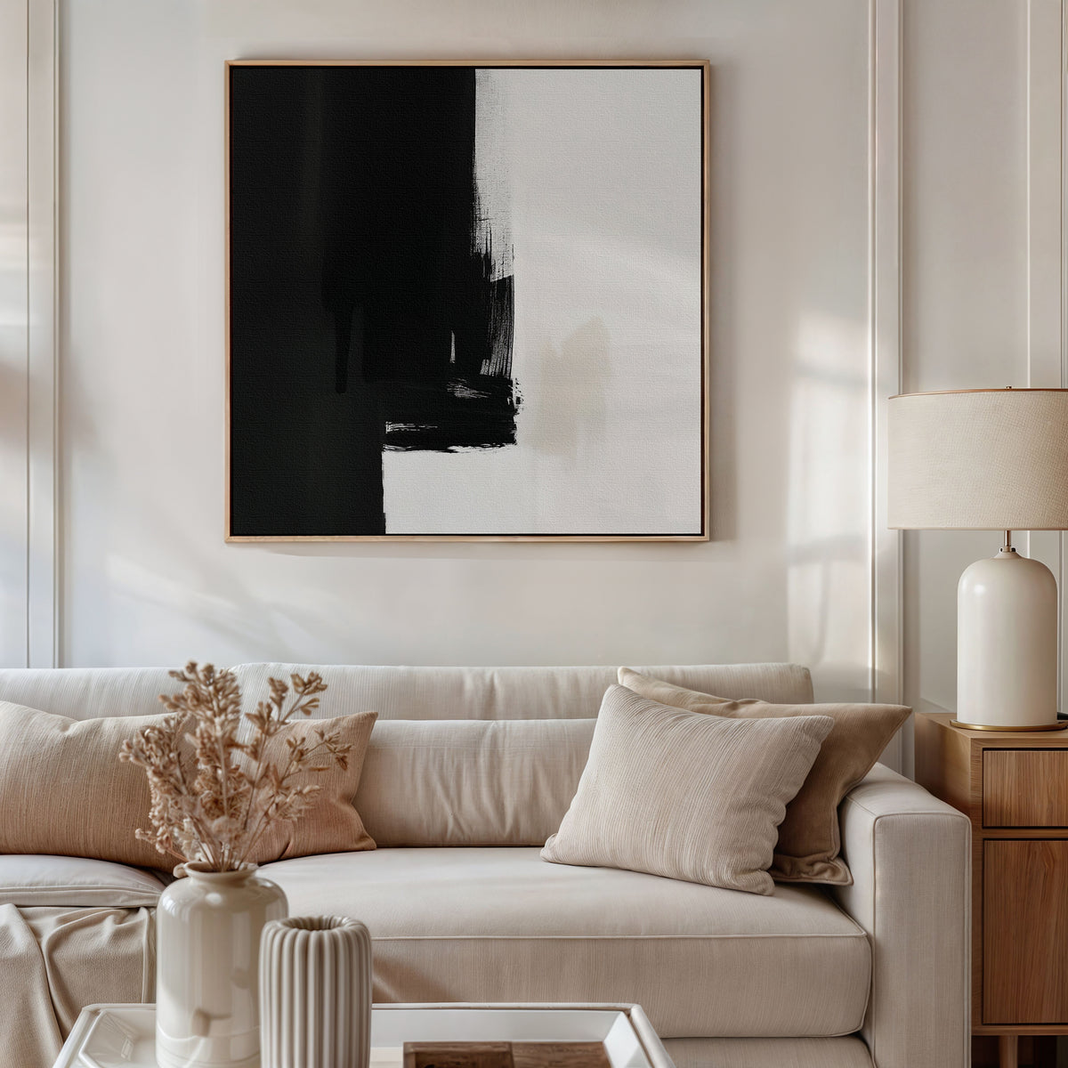 A modern living room with a beige sofa, neutral cushions, and dried flowers. Above the sofa hangs the Ink Divide Canvas Art - Square in black and white, adding Nordic Park-inspired elegance to the space.
