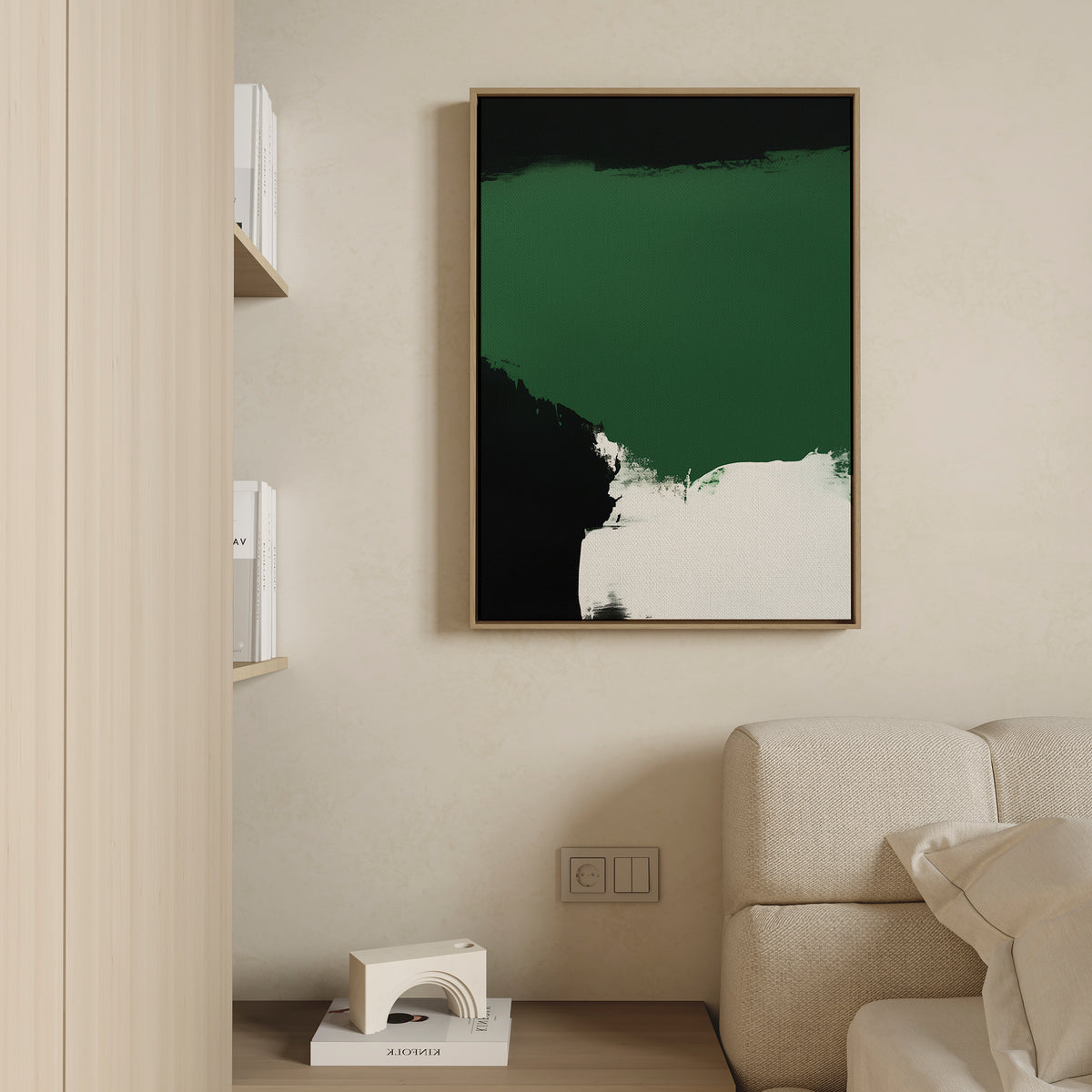 A minimal living room features a beige sofa, light wood shelves with books, and a modern touch— the Jade Depths Canvas Art - Vertical in emerald green, black, and white—plus a small geometric decor piece on the floor.