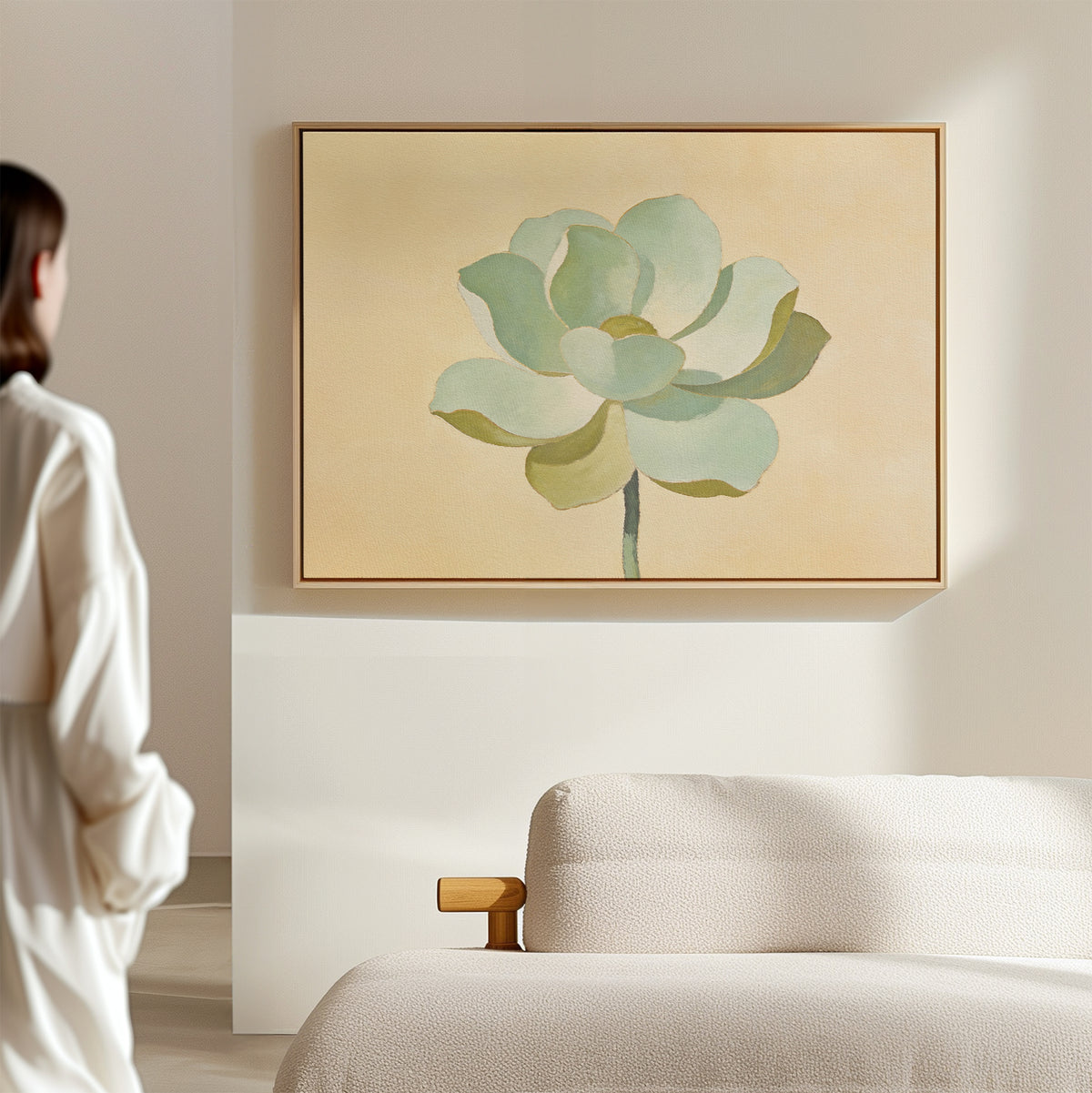 A person in white stands in a bright, minimal room, admiring the Jade Reflection Canvas Art - Horizontal—a botanical green flower print hanging above a beige sofa, adding the perfect minimalist wall art to the serene space.