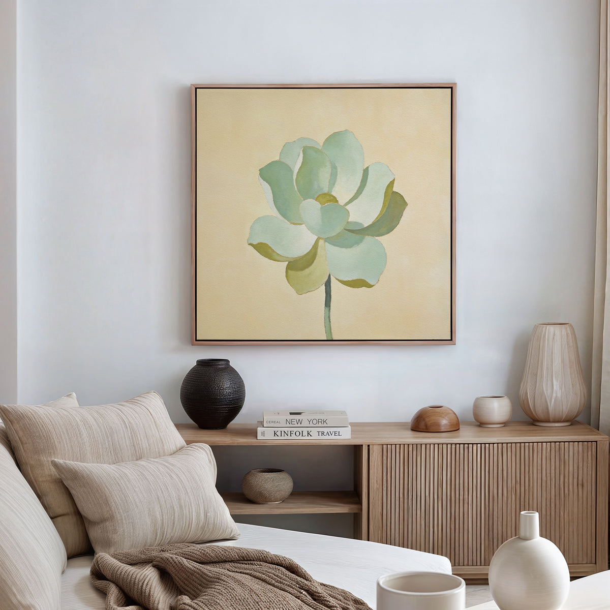 A minimal, modern living space featuring a beige sofa with neutral pillows, a wooden sideboard with vases and books, and the Jade Reflection Canvas Art - Square, a botanical print of a green succulent, displayed on the wall.