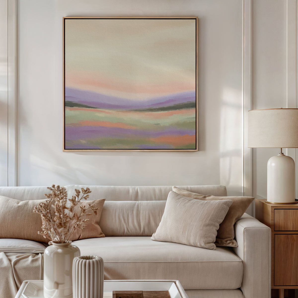 A modern living room features a beige sofa, neutral pillows, a light lamp, and vases with dried flowers on the table. Above the sofa hangs the Lavender Valley Canvas Art - Square, adding a serene and tranquil touch to the space.