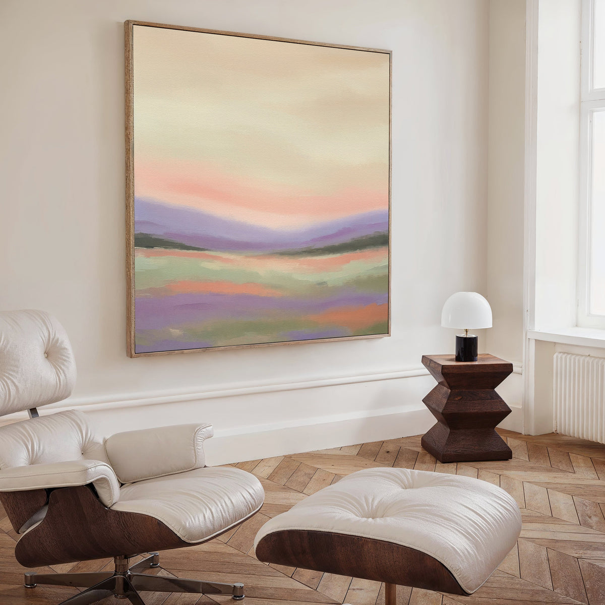 A modern living room with a white leather lounge chair and ottoman, a dark wooden side table with a small white lamp, and serene wall art—a square Lavender Valley Canvas Art—hanging above.