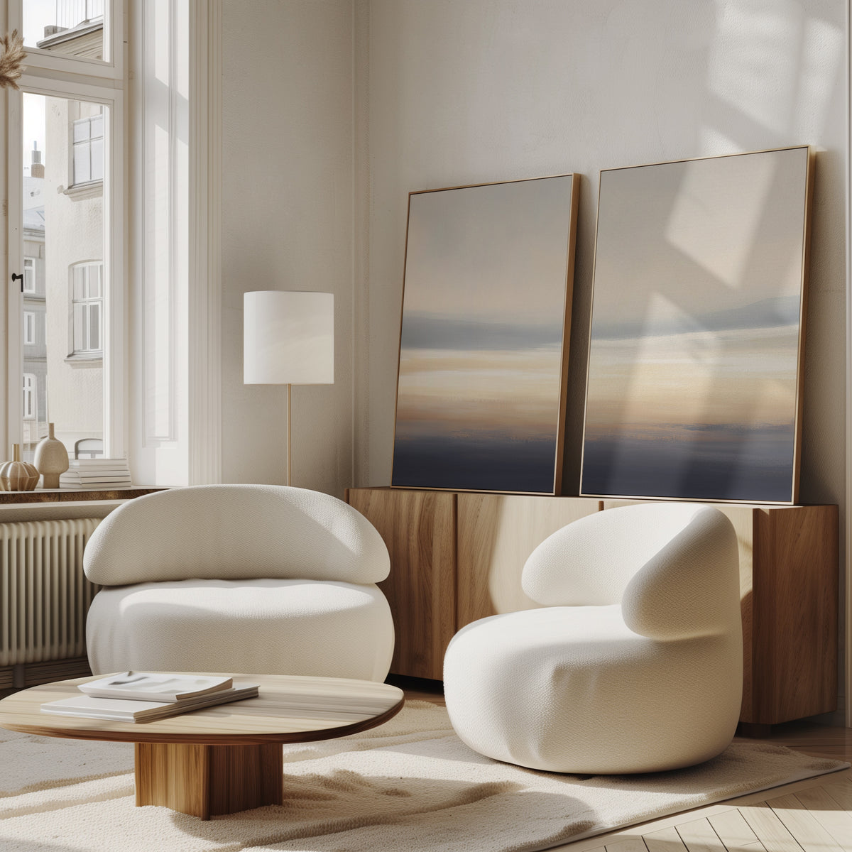 A modern living room featuring Layered Dusk - Set Of 2 rounded white armchairs, a low wooden coffee table, sideboard, abstract wall art, floor lamp, and large windows creates a serene atmosphere filled with natural light.