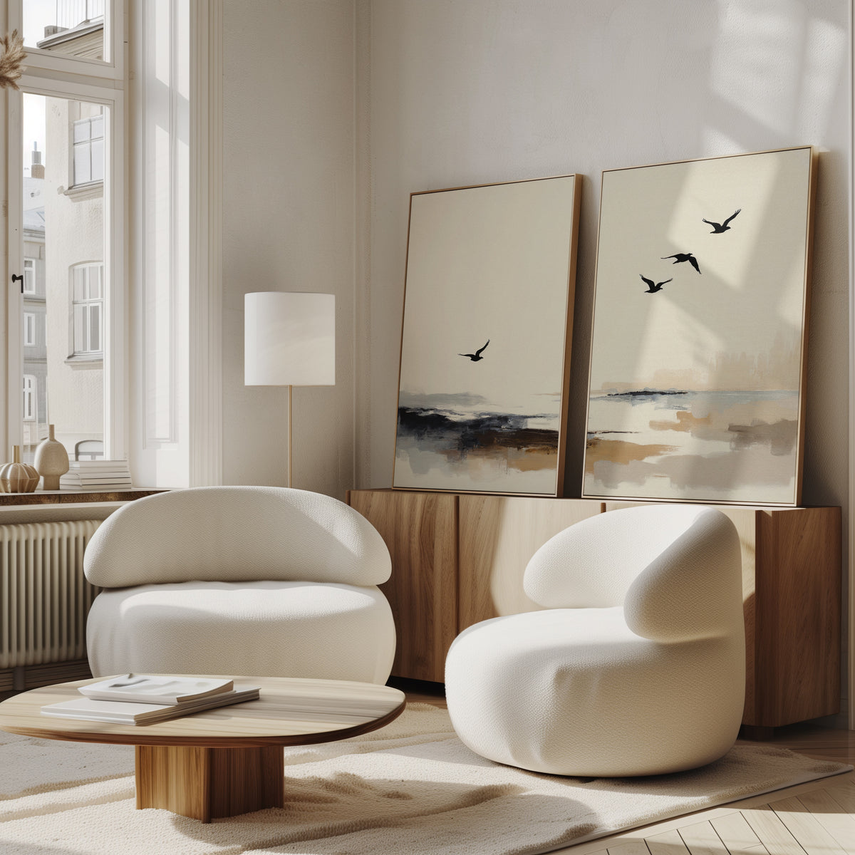 A modern living room with two white round armchairs, a wooden coffee table, and the Maritime Flight - Set Of 2 nautical bird wall art above a sideboard under tall windows filled with natural light.