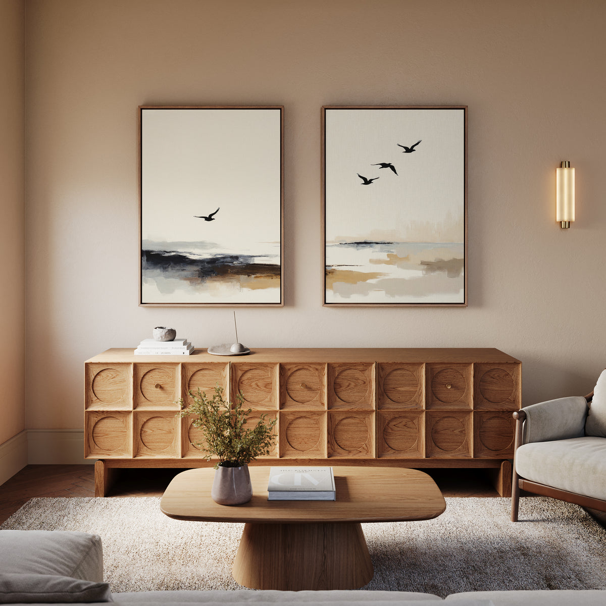 A minimalist living room with a wooden sideboard, coffee table, beige armchair, a small plant, soft wall lighting, and the Maritime Flight - Set Of 2 coastal bird prints on the wall creates a warm, cozy atmosphere.