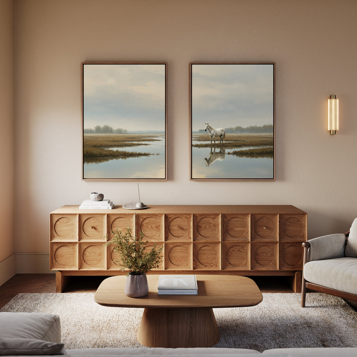 A cozy living room with a modern wooden sideboard, a round coffee table, a light gray sofa, and the Marsh Reflection - Set Of 2 serene landscape prints with white horse artwork above the sideboard. A small vase with greenery sits on the table.