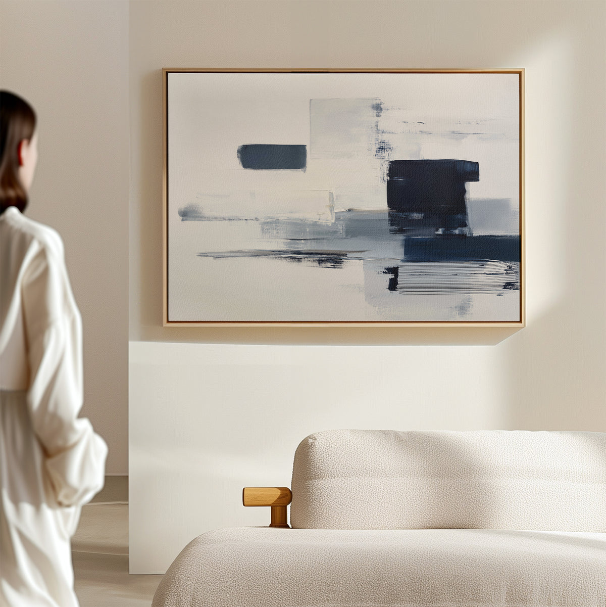 A person stands by a beige sofa, admiring the Navy Brushwork Canvas Art - Horizontal, featuring bold blue and white strokes, framed on a light wall in a modern minimalist room.
