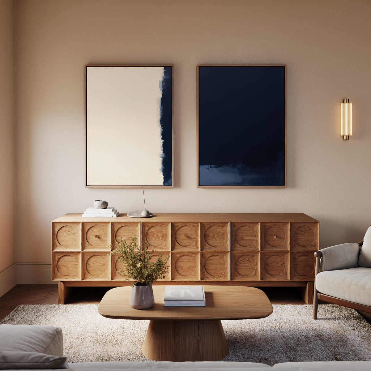 A modern living room with a wooden sideboard, low coffee table, beige armchair, and two abstract paintings—Navy Division - Set Of 2—hanging above, complemented by a wall sconce for soft lighting and modern elegance.