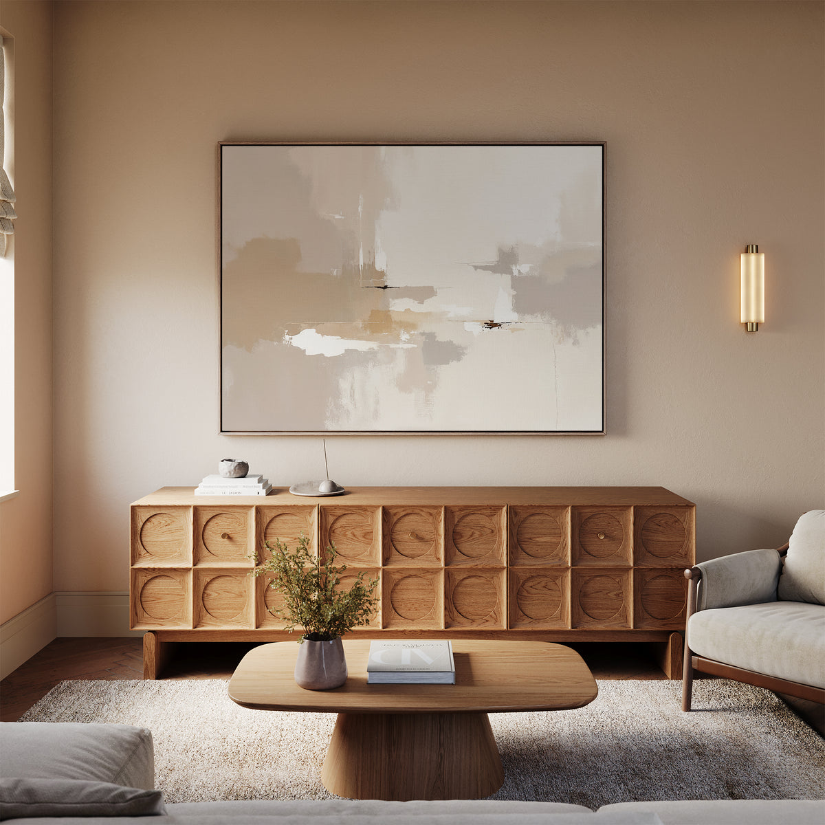 A modern living room features the Neutral Territory Canvas Art - Horizontal above a wooden sideboard, with a beige sofa, minimalist decor, a wooden coffee table topped with books and flowers, and a textured neutral-toned rug.