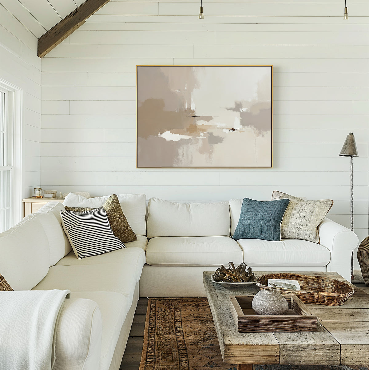 A cozy living room features a white sectional sofa, assorted pillows, a rustic wooden coffee table with decor, and the Neutral Territory Canvas Art - Horizontal adding contemporary elegance to the white shiplap wall in soft natural light.