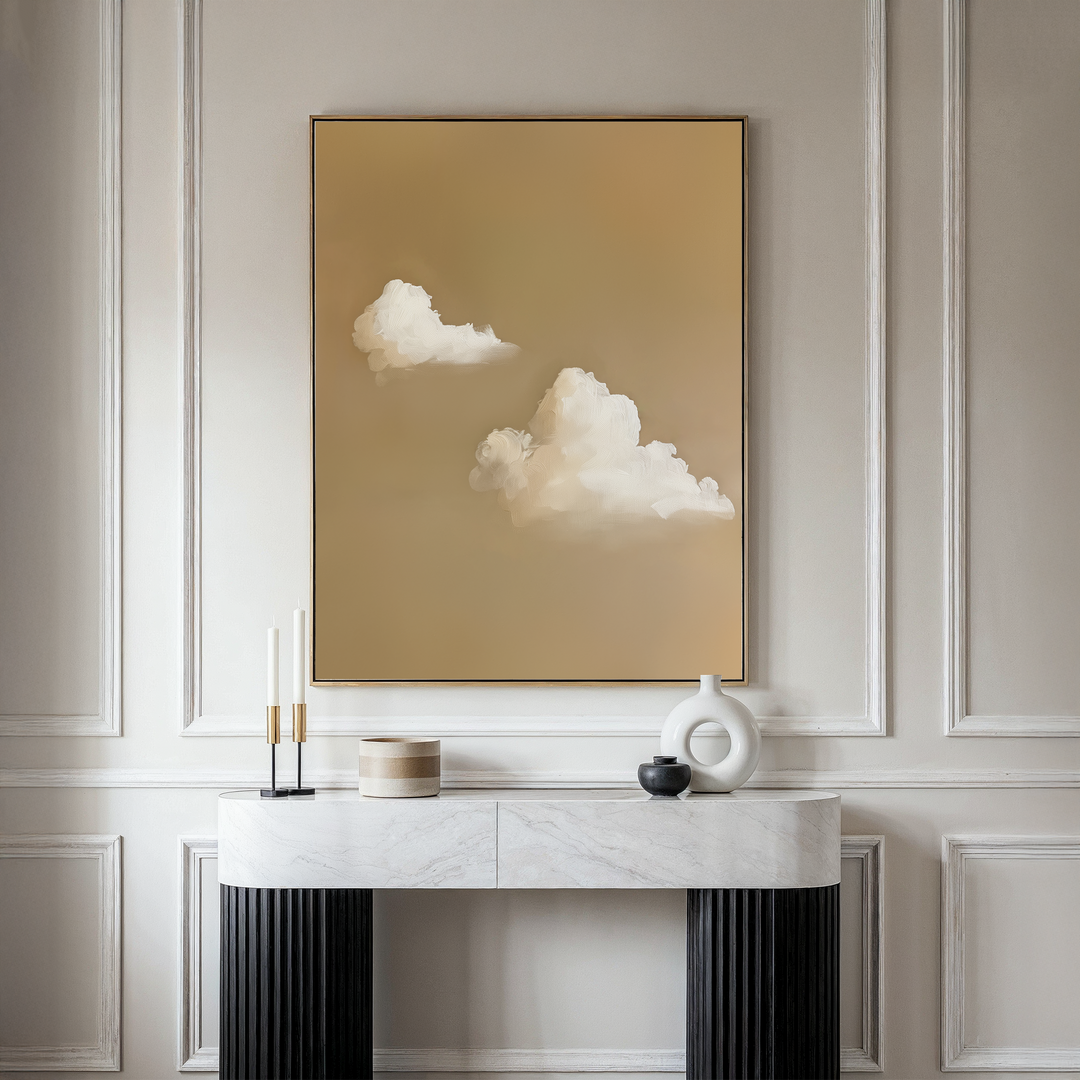 A minimalistic living space featuring the Whispering Clouds large framed wall art—white clouds on beige—a marble console table with black legs, and chic decor accents, ideal for a refined living room style.