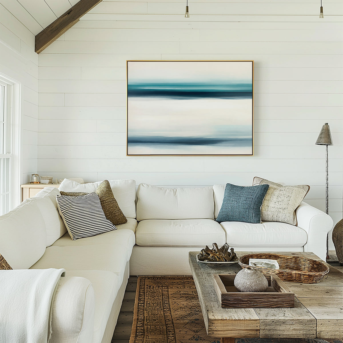 A bright living room with a white sectional sofa, mixed pillows, a rustic wooden coffee table, and the Ocean Motion Canvas Art - Horizontal on the shiplap wall exudes serene sophistication as warm light streams in from the left.