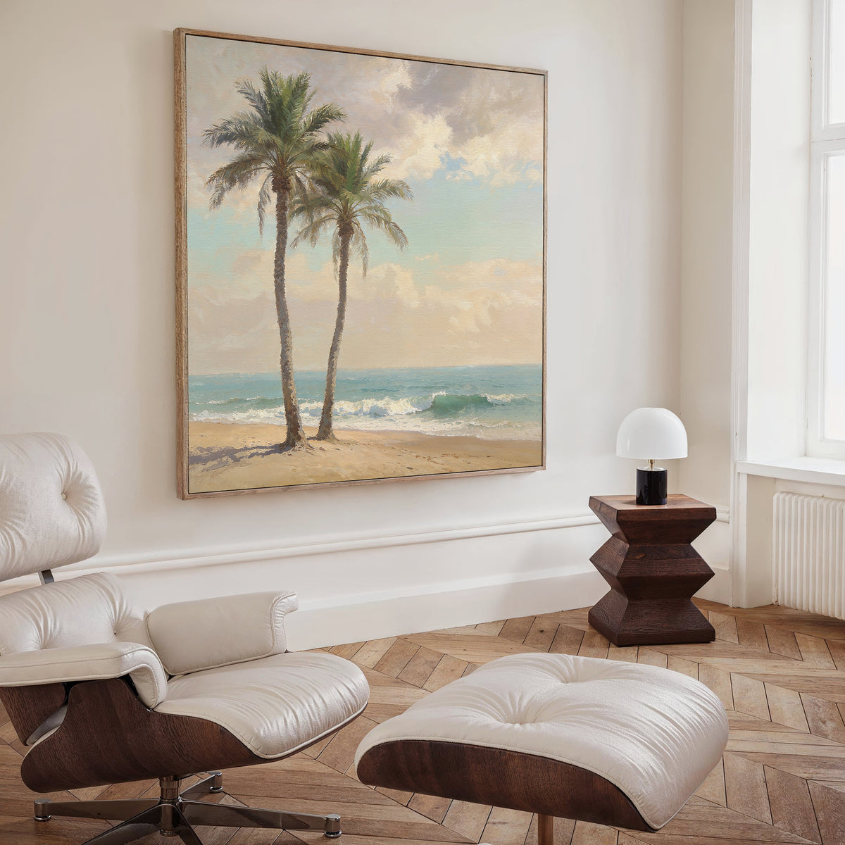 A cozy, modern living room with a white lounge chair and ottoman, a small wooden side table with a white lamp, and the Paradise Found Canvas Art - Square—a serene tropical beach scene—hanging above.