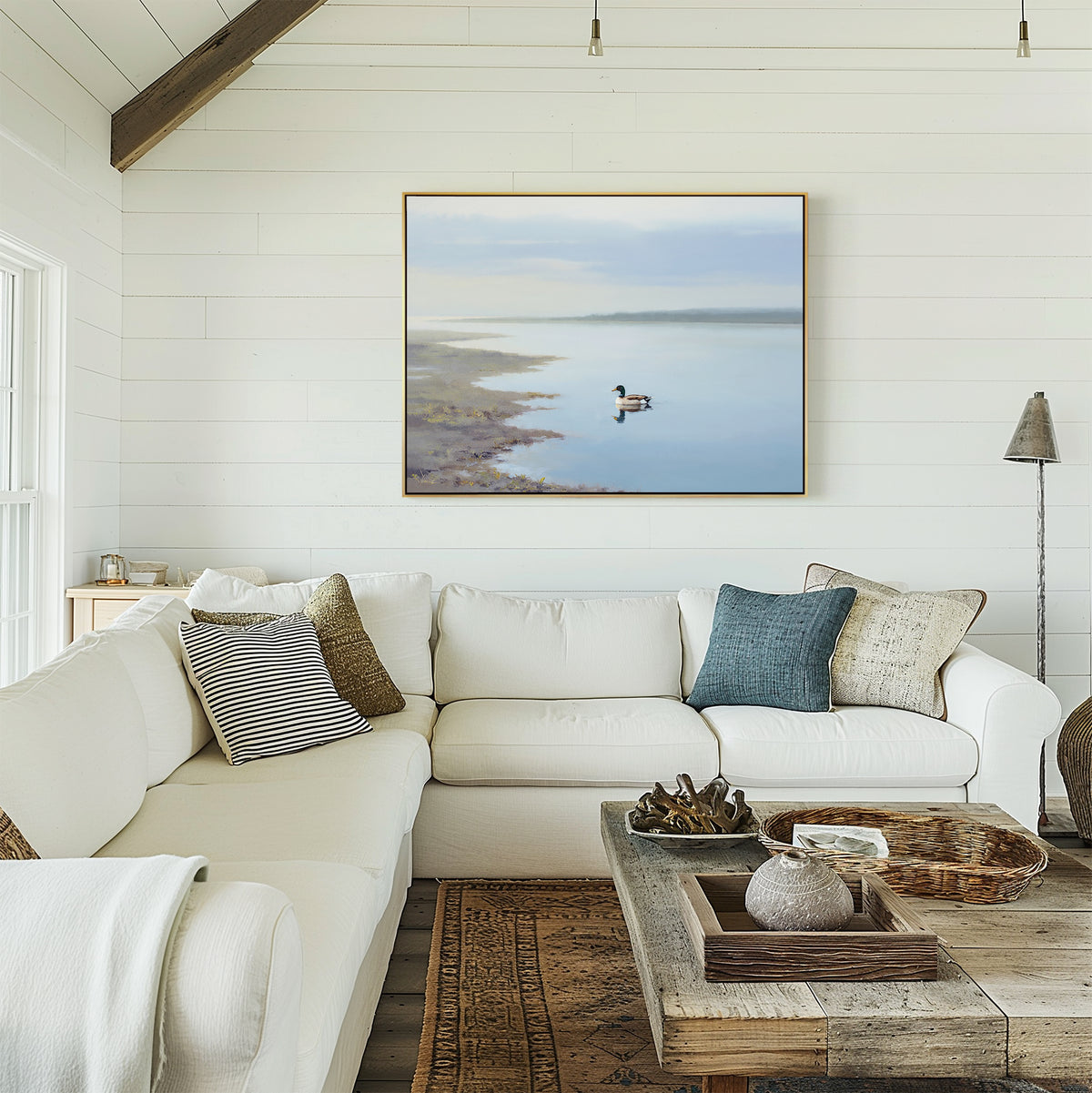 A bright, cozy living room with white shiplap walls, a large white sectional sofa with assorted pillows, a rustic wooden coffee table, and the Peaceful Duck Haven Canvas Art - Horizontal displayed above the couch.