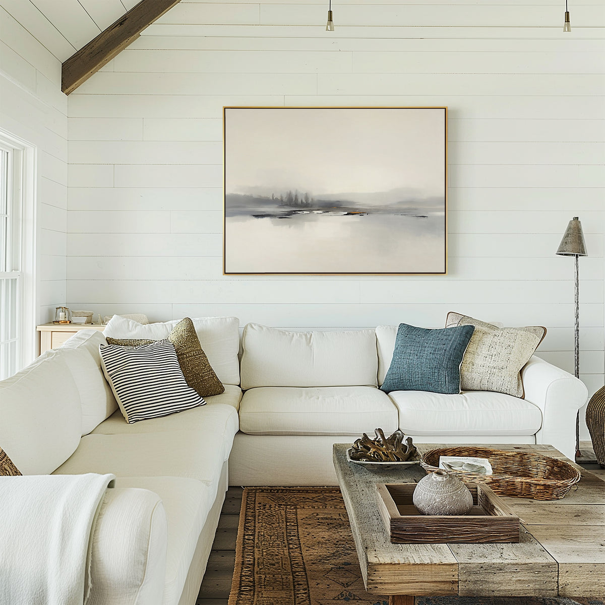 A bright, cozy living room with a white sectional sofa, assorted throw pillows, and a rustic wooden coffee table. The Peaceful Lake Morning Canvas Art - Horizontal hangs on the white shiplap wall above the sofa for a serene touch.