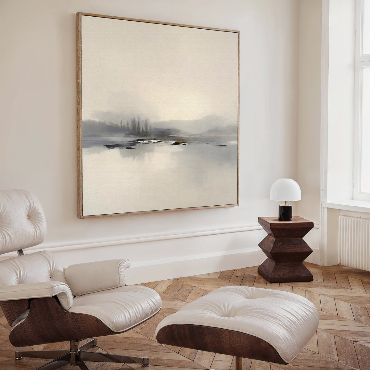A minimalist living room with a white leather lounge chair and ottoman, modern wood side table, white table lamp, and the Peaceful Lake Morning Canvas Art - Square above light herringbone flooring creates a serene atmosphere.