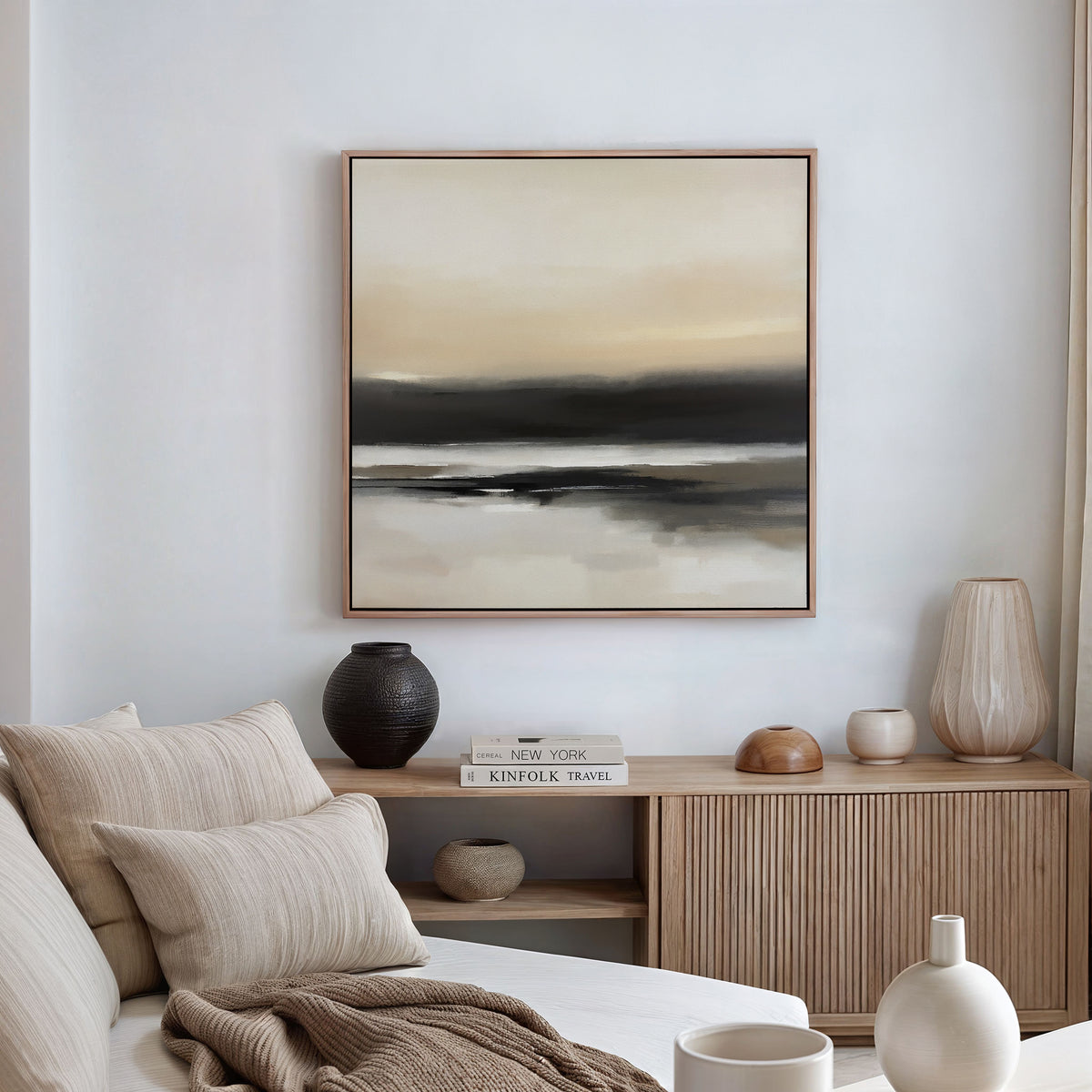 A minimalist living room features the Quiet Shoreline Canvas Art - Square above a wooden sideboard with vases, books, and ceramics. A beige sofa with pillows sits in the foreground, completing the refined minimalist decor.