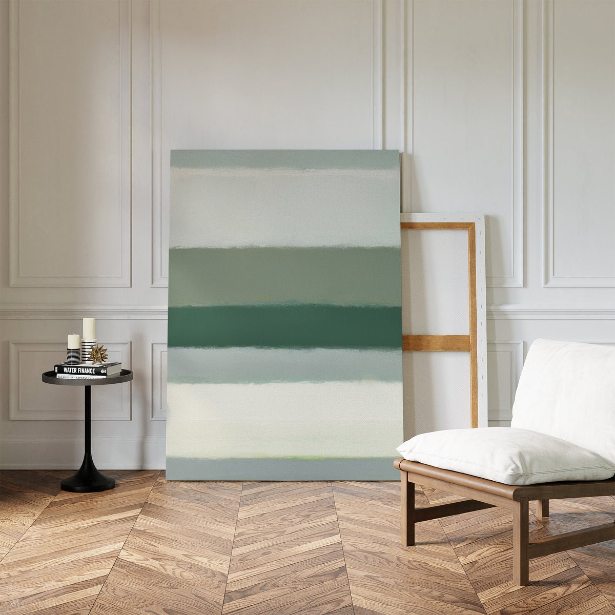 A minimalist room with chevron wood floors, white paneled walls, a cushioned chair, a round black side table with candles, and the Sage Gradient Canvas Art - Vertical in calming green tones leaning against the wall.