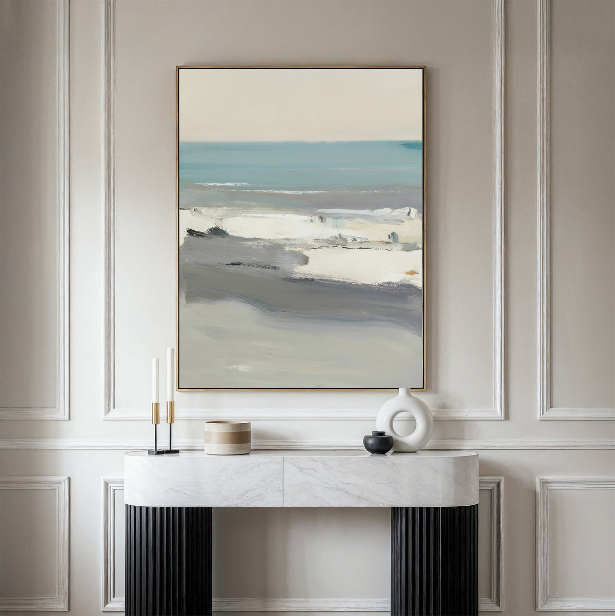 The Sandy Retreat Canvas Art - Vertical hangs on a white paneled wall above a white marble console table with black legs, styled with minimalist objects and candles for subtle seaside vibes.