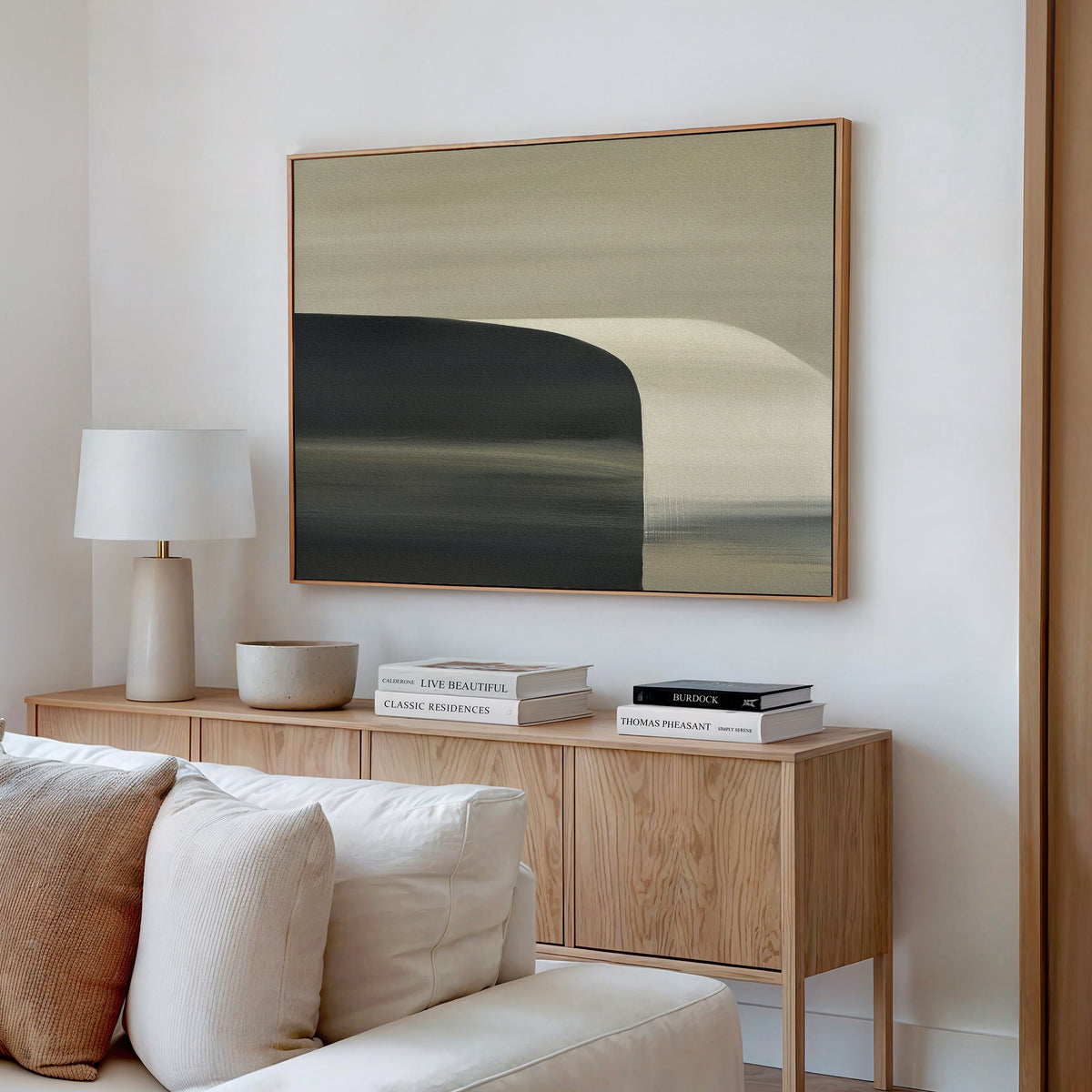 A modern living room with minimalist decor features a light wood sideboard, books, a lamp, decorative objects, and the Sculptural Forms Canvas Art - Horizontal in earthy tones hanging above a beige sofa on a white wall.