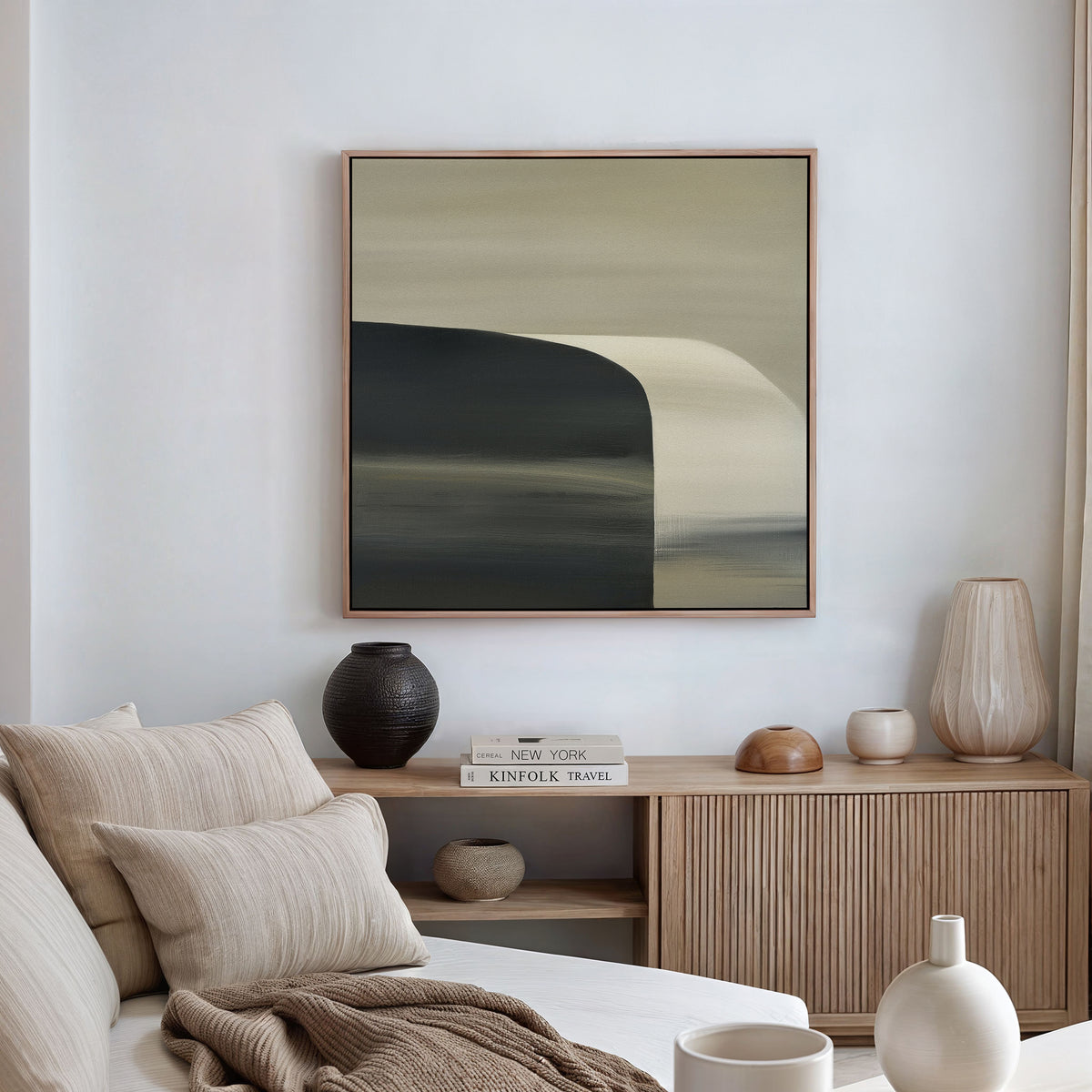 A modern living room with minimalist decor features a beige sofa and cushions, a wooden sideboard topped with books and vases, and the Sculptural Forms Canvas Art - Square in neutral tones hanging on the wall.