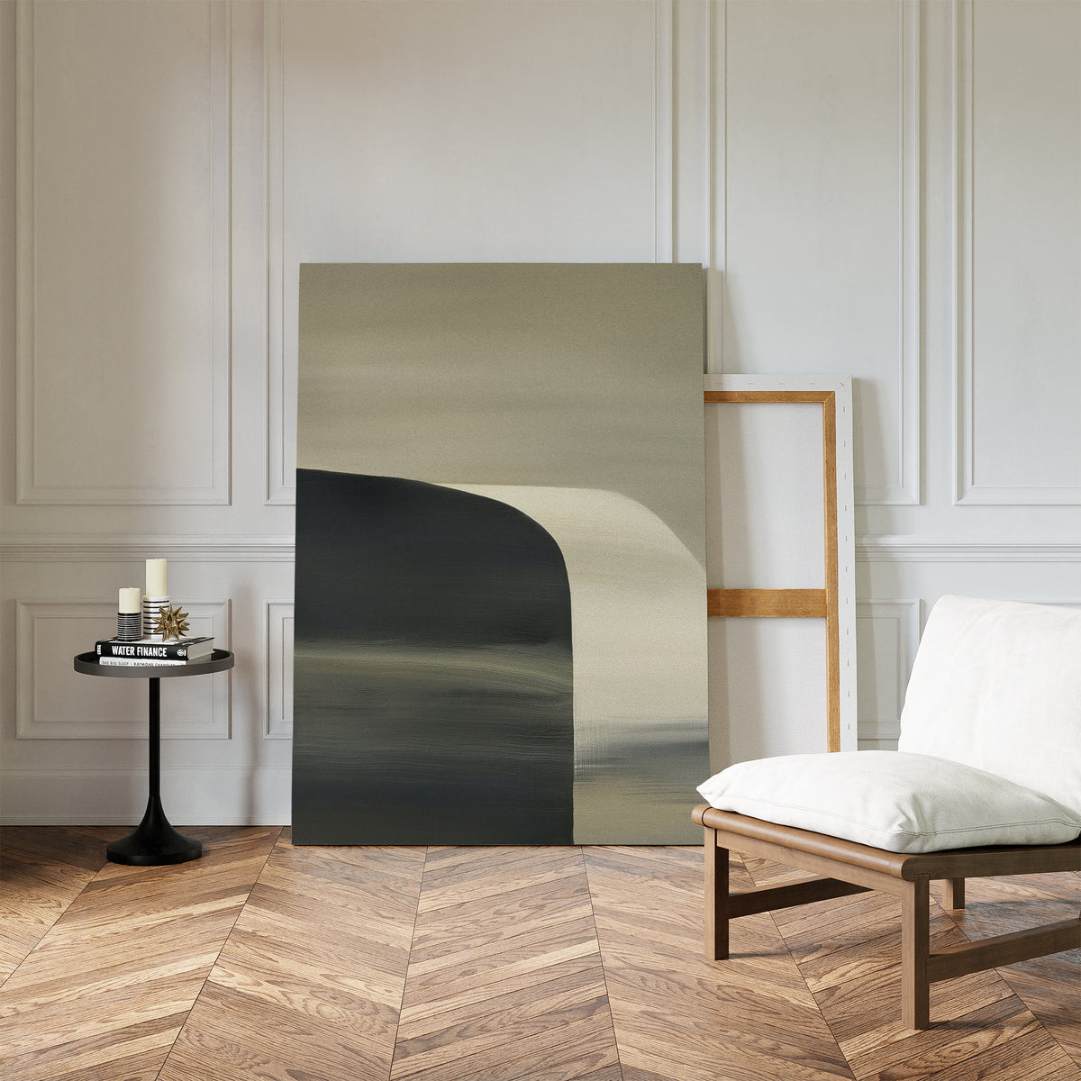 A minimalist setup with herringbone wood floors, a white cushioned chair, a small black round side table with candles and books, and the Sculptural Forms Canvas Art - Vertical leaning against a white paneled wall—ideal for modern living rooms.
