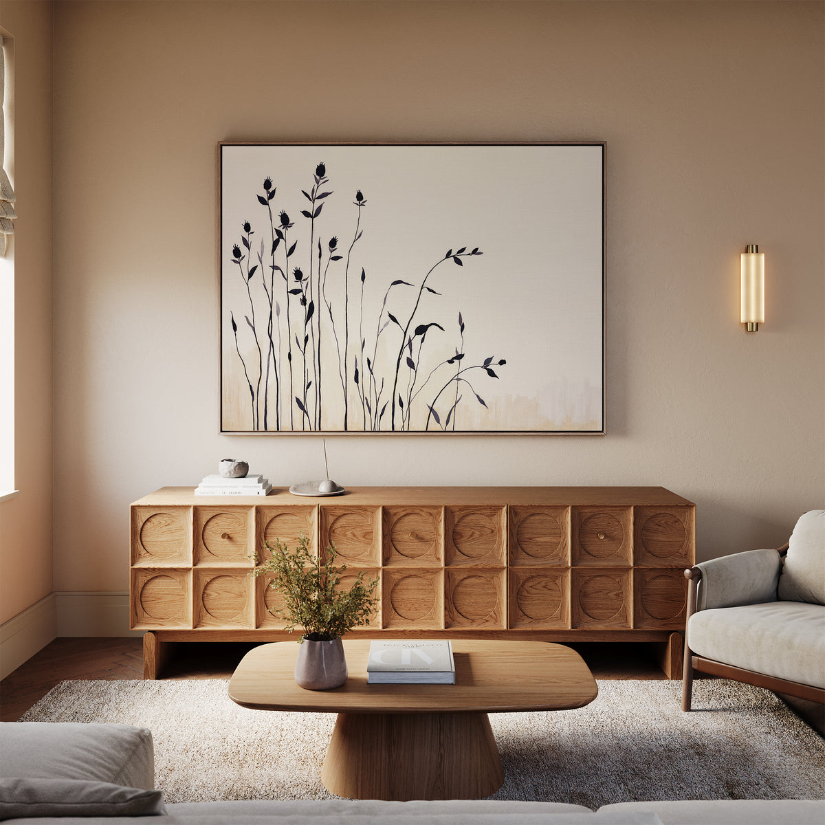 A cozy living room with neutral tones features a wooden sideboard with circular patterns, the Silhouette Meadow Canvas Art - Horizontal above it, a modern coffee table, a light sofa, and a small plant in a vase.