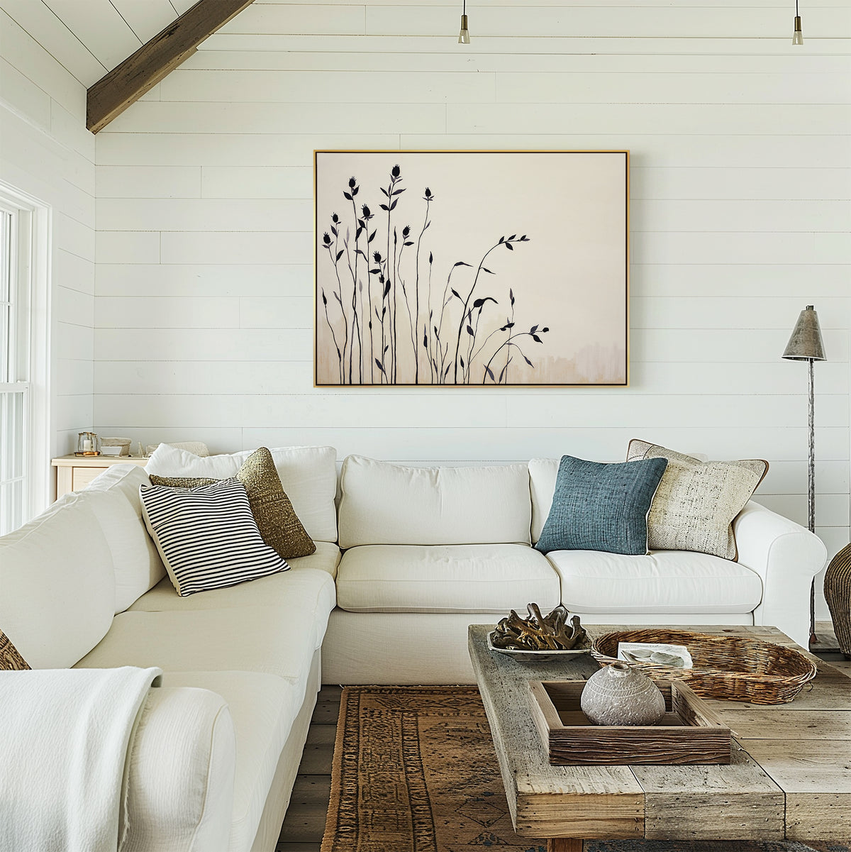 A cozy living room with white shiplap walls, a white sectional sofa and assorted pillows, a rustic wood coffee table, and the Silhouette Meadow Canvas Art - Horizontal above the couch. Natural light brightens this inviting Nordic-inspired space.