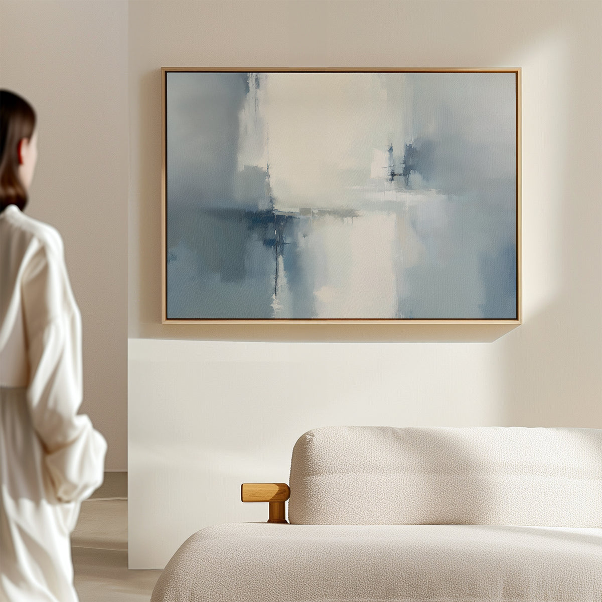 A person in a white shirt stands in a bright, minimalist room, admiring the Silver Cross Formation Canvas Art - Horizontal in blue and white tones above a beige sofa, adding striking modern style to the living room decor.