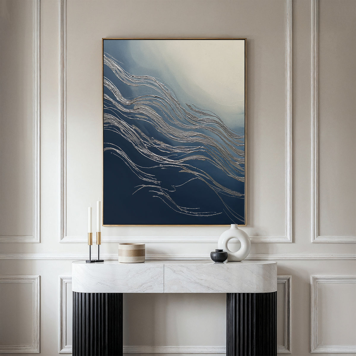 The Silver Current Canvas Art - Vertical, with its blue, white, and gold wave-like patterns, hangs above a minimalist console table with decorative items, bringing contemporary sophistication to the elegant modern room.